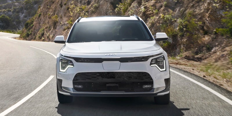 front grille of white 2024 kia niro ev driving down hilly road