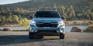 frontal view of blue-green 2024 Kia Seltos parked with a lake and mountain behind
