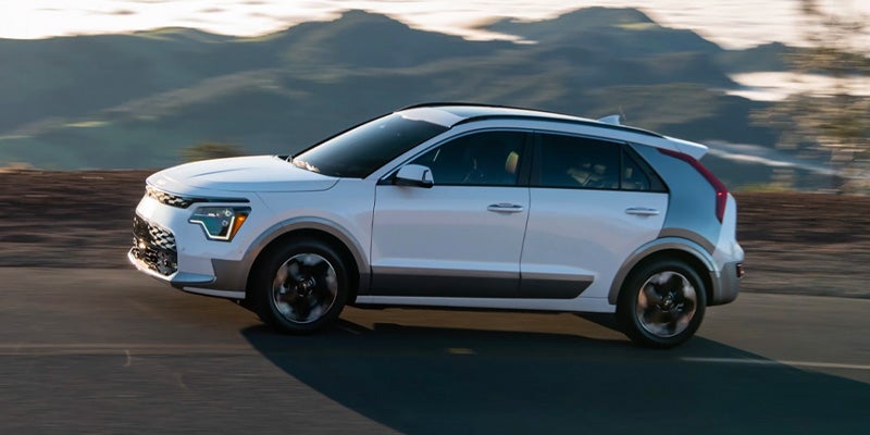 white kia niro ev driving down country road with blurred mountain range in the backdrop