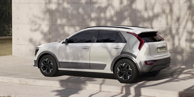 white 2024 kia niro ev parked by a building wall under the shade of some branches